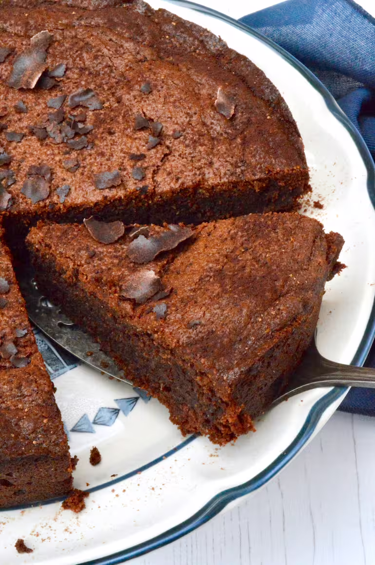 Slice of chocolate almond cake being removed from remaining cake.