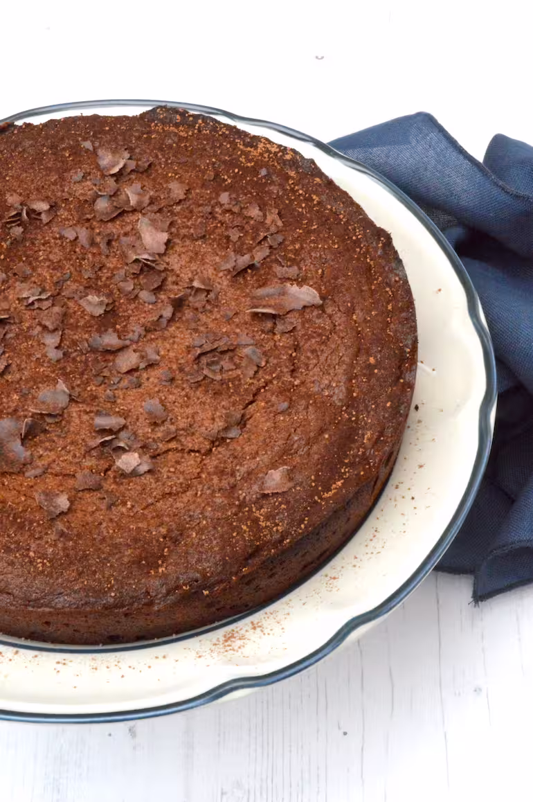 Partial view of chocolate almond cake on plate with chocolate shavings on top.