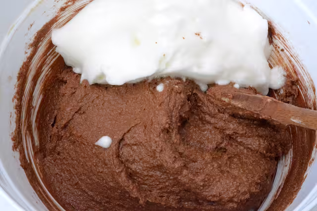 Whisked egg whites added to chocolate mix in bowl.