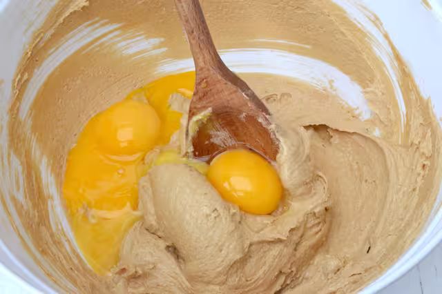 Egg yolks added to creamed butter and sugar in bowl with wooden spoon.
