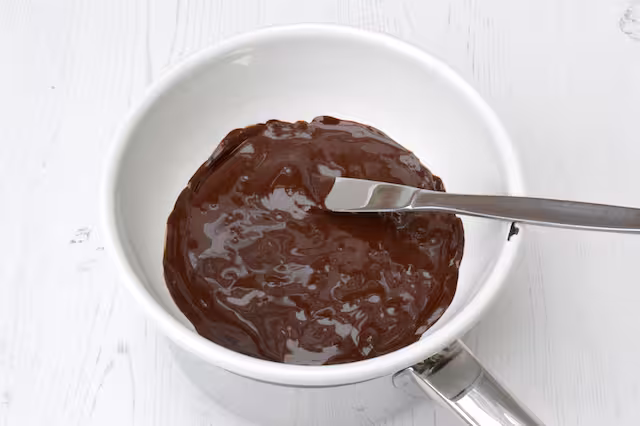 Melted chocolate in a bowl over hot water with knife.