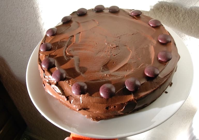 A round sour cream chocolate cake covered in ganache and chocolate button decorations.