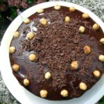 An iced hazelnut chocolate cake on a white plate.