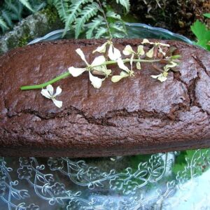A loaf of chocolate prune gingerbread with a stem of rocket flowers lying on top.