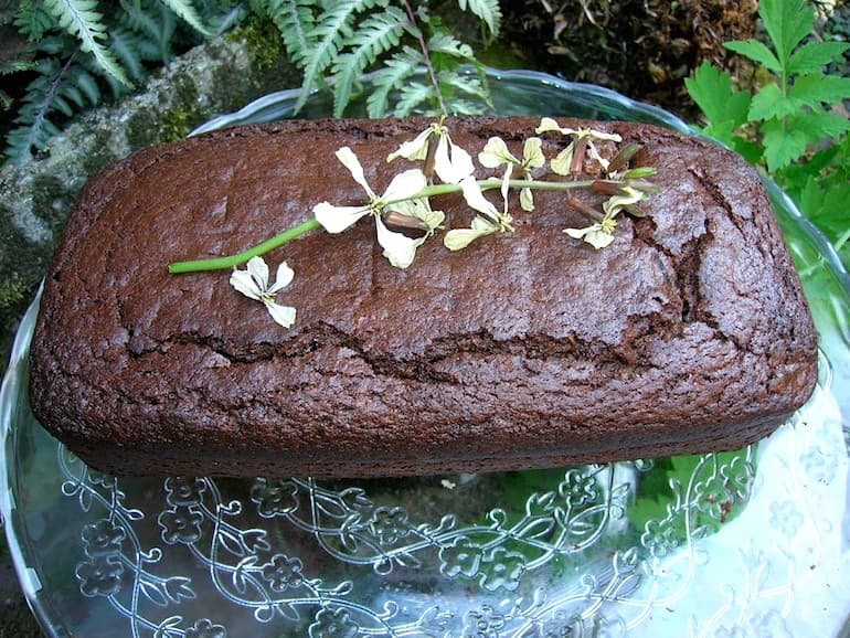 A loaf of chocolate prune gingerbread with a stem of rocket flowers lying on top.