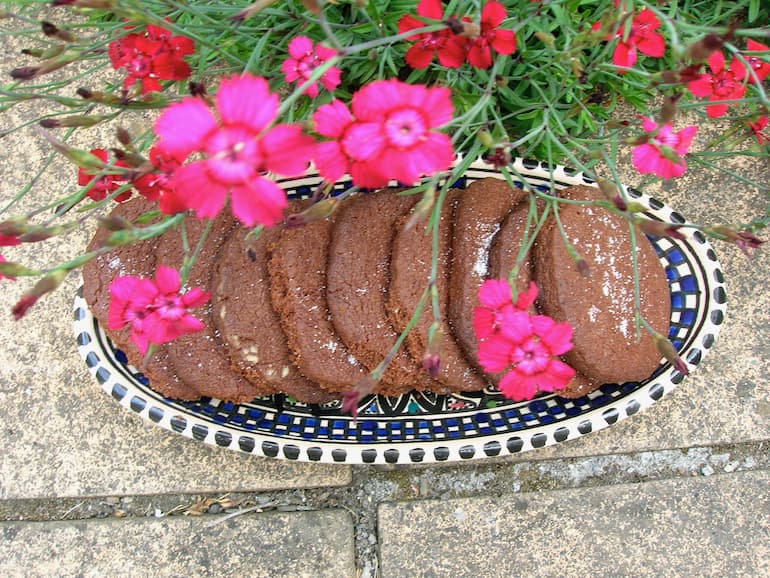 A platter of chocolate and cardamom shortbread biscuits wit flowers.