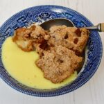 A bowl of chocolate chip apple crumble with custard.