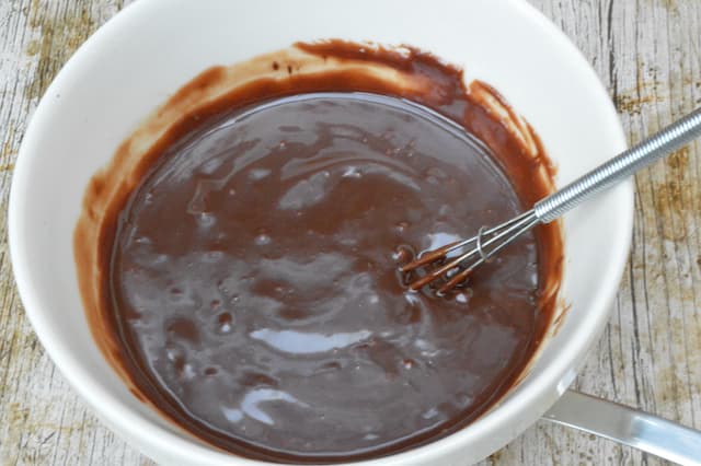Liquid ganache in a bowl with whisk.