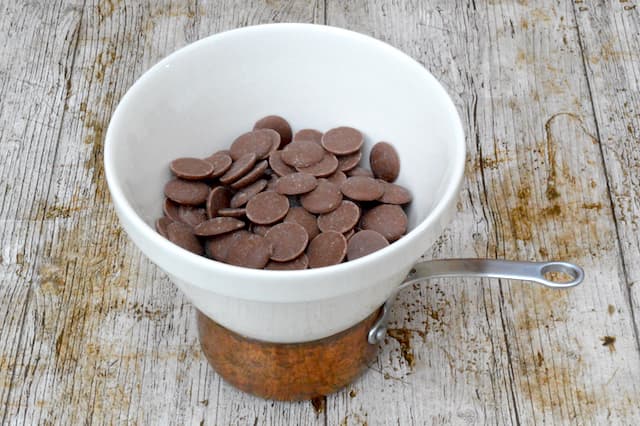 Milk chocolate buttons in a bowl sitting atop a small pan of water.