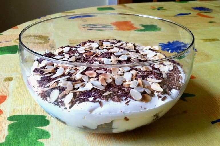A glass bowl of leftover cake trifle with grated chocolate and toasted almond flakes on top..