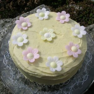 Lime and white chocolate genoise sponge cake covered in lime and white chocolate icing with wafer daisies on the top.