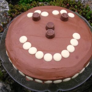 A chocolate rolo cake with a smiley face made out of white chocolate buttons and rolos.