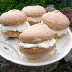 Four rose meringues sandwiched with white chocolate cream on a plate.