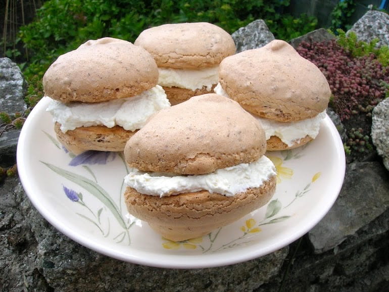 Four rose meringues sandwiched with white chocolate cream on a plate.