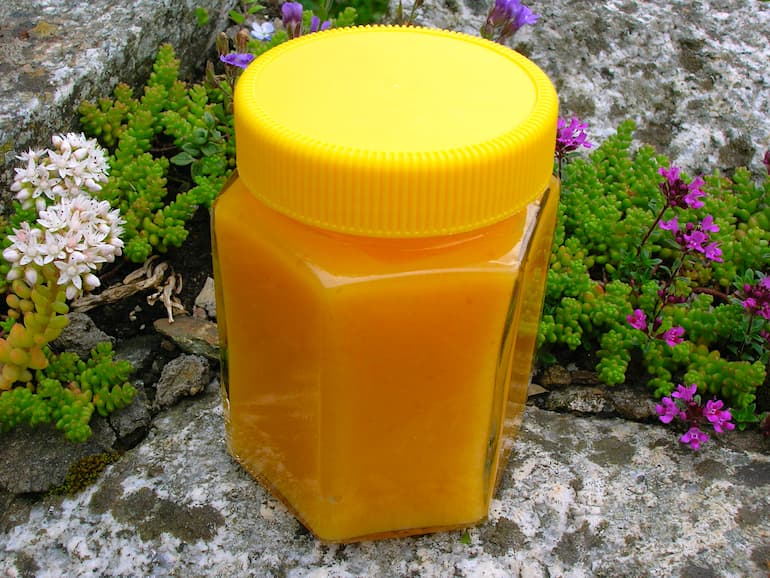 A yellow lidded jar of apricot curd sitting on a stone wall.