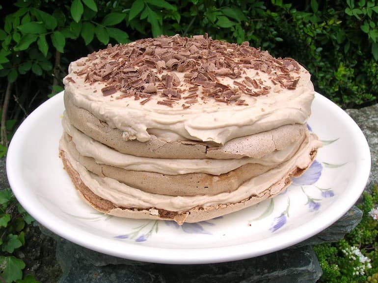 A three layered chestnut cream meringue cake topped with chocolate shavings on a plate.