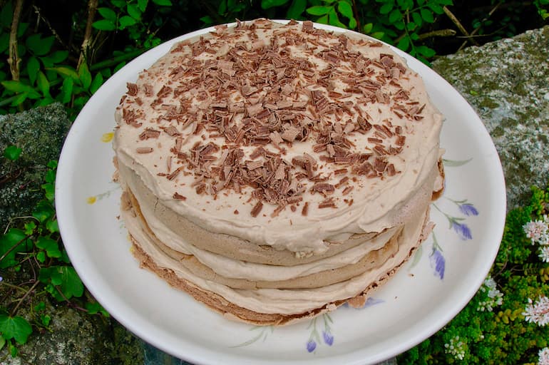 A three layered chestnut cream meringue cake topped with chocolate shavings on a plate.