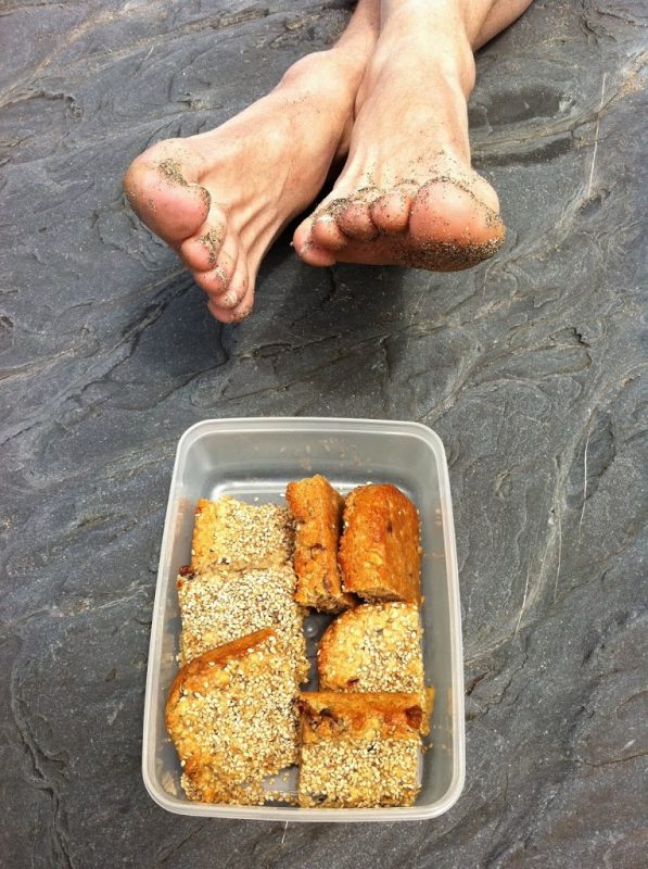 Halva flapjacks in a container with a pair of feet in the background.