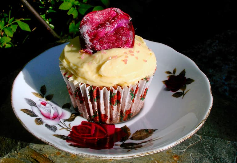 A rose patterned saucer with a single chocolate rose cupcake covered in rose buttercream with a crystallised rose petal perched on top.