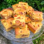 Squares of plum and chocolate cheesecake traybake piled on plate.