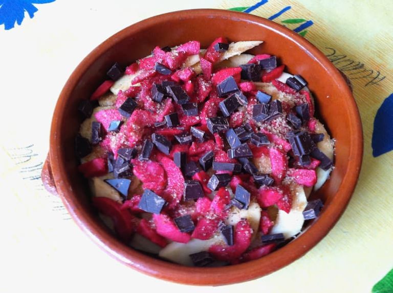 A baking dish of red fleshed apple slices and chocolate for a brown betty.