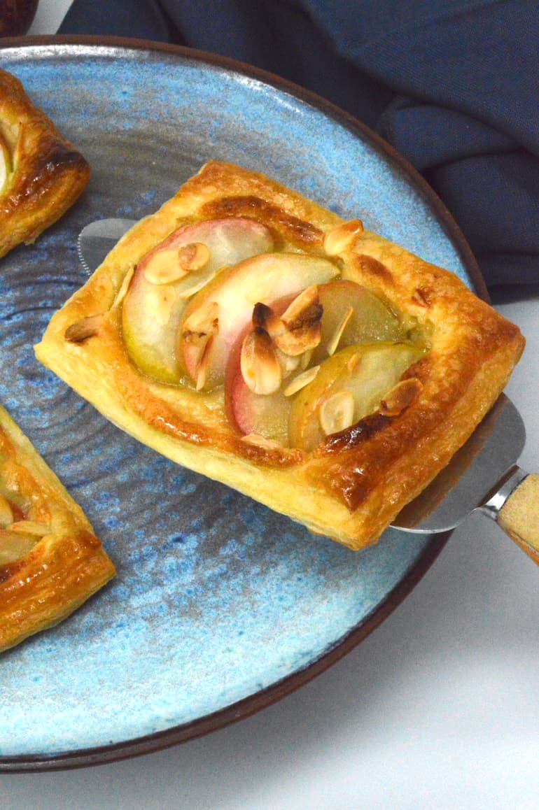 An apple and almond Danish-type pastry lifted from a plate.