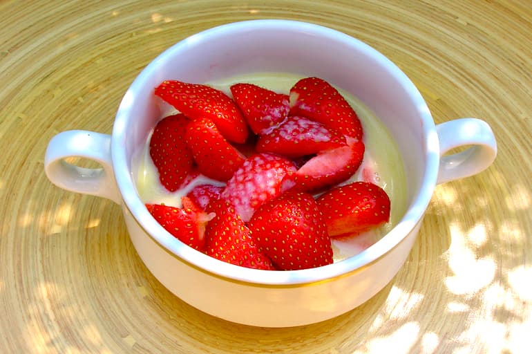 A bowl of slices strawberries in white chocolate sauce.