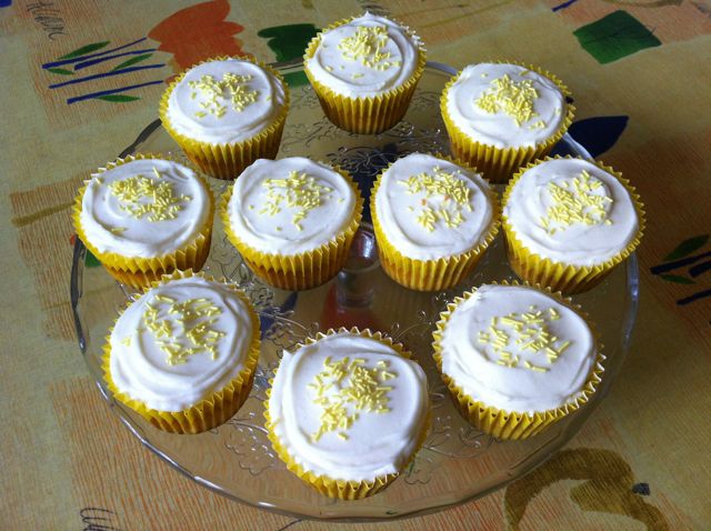Lemon and white chocolate cupcakes sitting on a glass cake stand.