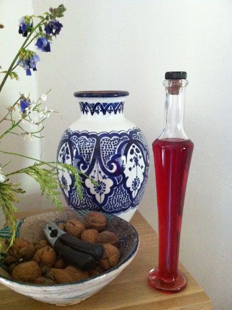A bottle of rose syrup with a bowl of nuts and a vase.