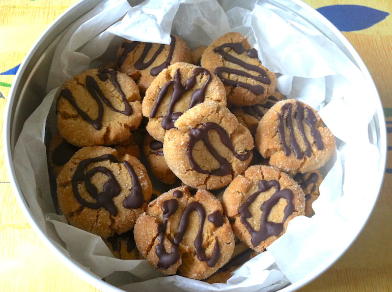 A tin of peanut butter thumbprint cookies drizzled with chocolate.