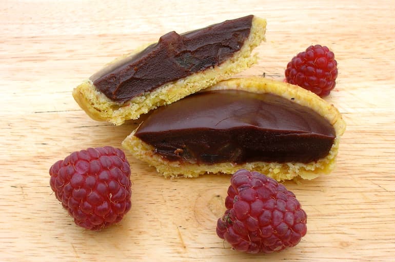 Two halves of a fennel and ginger chocolate tart with raspberries.