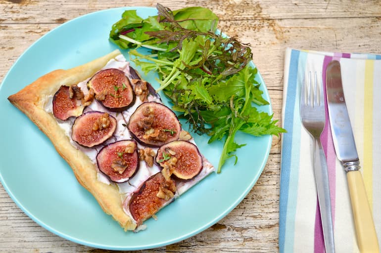A slice of honeyed gig & goat's cheese tart with walnuts, thyme and chocolate balsamic with a side of green leaves.