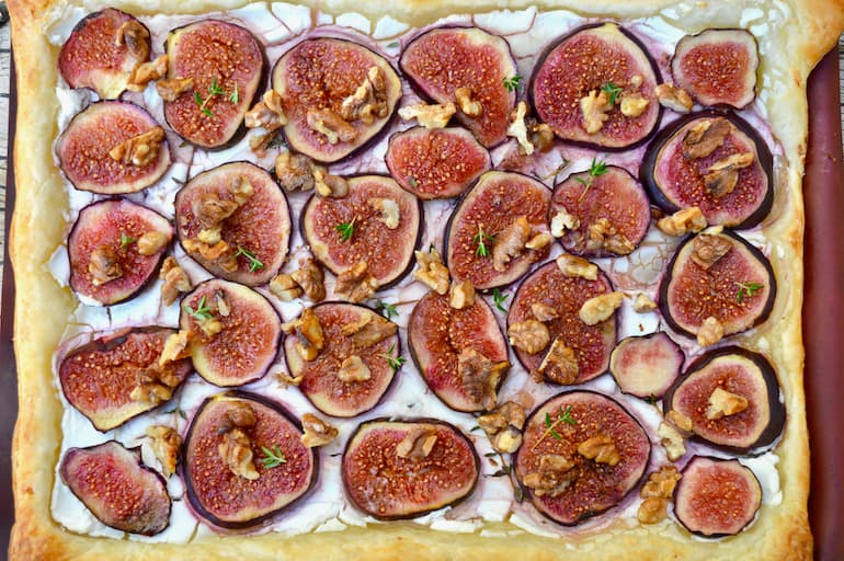 Close up of a sliced figs on puff pastry with walnuts, thyme and honey.