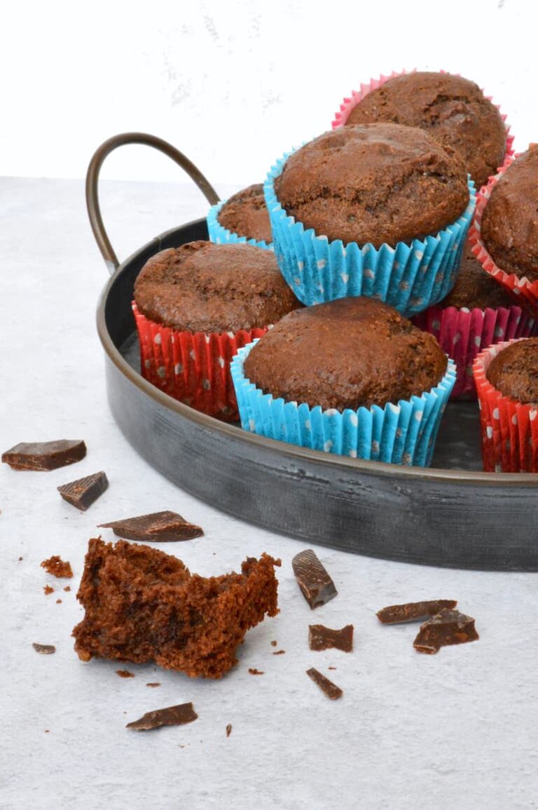 Vegan Mexican chocolate muffins piled onto tray with sponge and chocolate pieces on side.