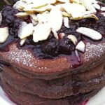 A stack of chocolate pancakes topped with blackcurrant compote and flaked almonds.