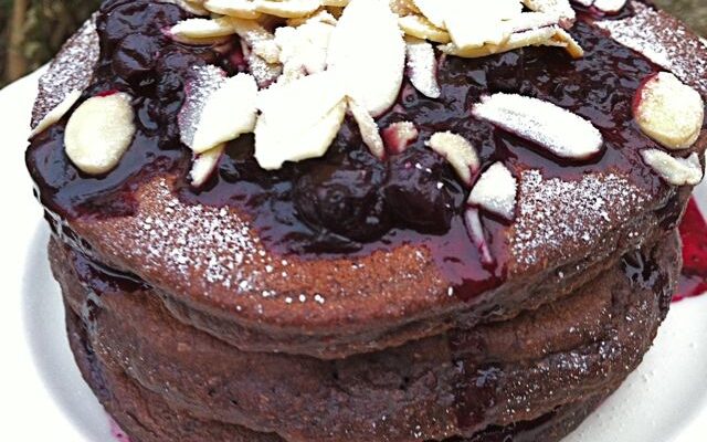 A stack of chocolate pancakes topped with blackcurrant compote and flaked almonds.