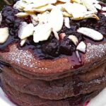 Stack of chocolate pancakes topped with blackcurrant compote and flaked almonds.
