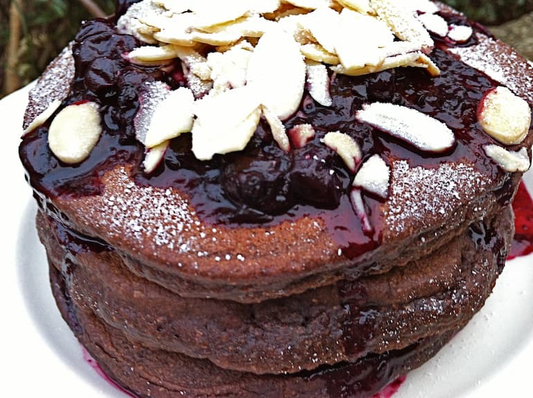 Stack of chocolate pancakes topped with blackcurrant compote and flaked almonds.