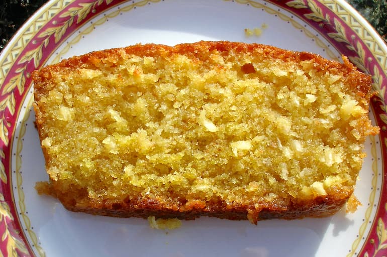 Slice of coconut and lime drizzle loaf cake on plate.
