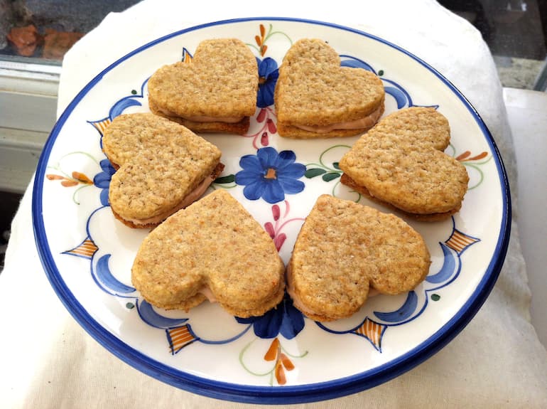 Plate of heart shaped coffee biscuits sandwiched with whipped coffee chocolate ganache.
