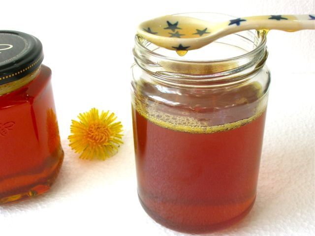 A jar of dandelion honey with a dripping spoon.