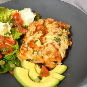 Two vegetarian enchiladas on a grey plate with avocado and salad.