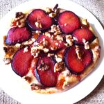 A baked plum and walnut dessert pizza on a white plate.