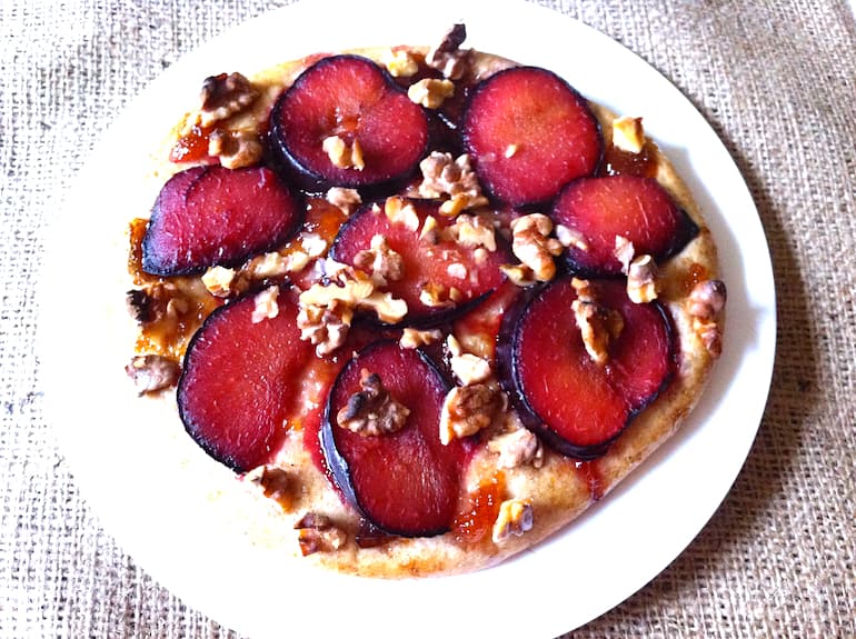 A baked plum and walnut dessert pizza on a white plate.