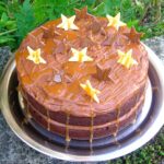 A salted caramel chocolate cake on a silver tray sitting on an ourdoor wall. Decorated with white and milk chocolate stars.