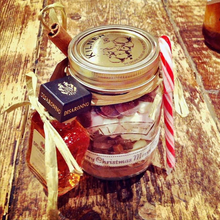 Hot chocolate ingredients layered up in a glass jar with candy cane and bottle of Amaretto.