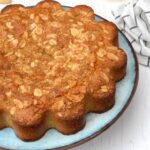 Partial view of lemon almond cake on plate with lemons and almonds on side