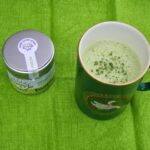 A mug of Matcha Hot Chocolate and a tub of matcha green tea powder.