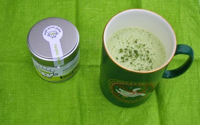 A mug of Matcha Hot Chocolate and a tub of matcha green tea powder.