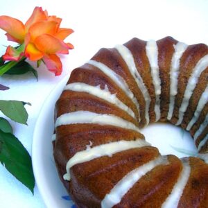 Partial view of a striped banana bundt cake with an orange rose on the side.